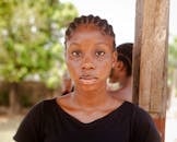 Close-up portrait of a woman wearing a black shirt with cornrow hairstyle, outdoors, under natural light.