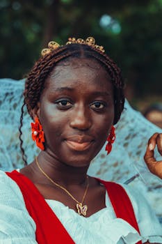 Close-up portrait of a young Ghanaian woman in traditional attire with braided hair and colorful accessories.